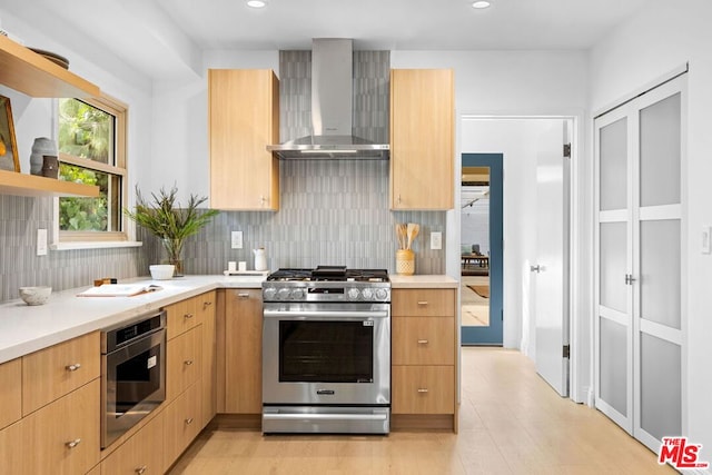 kitchen with light brown cabinetry, decorative backsplash, gas stove, and wall chimney exhaust hood