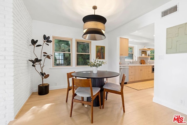 dining room with brick wall, plenty of natural light, and light wood-type flooring