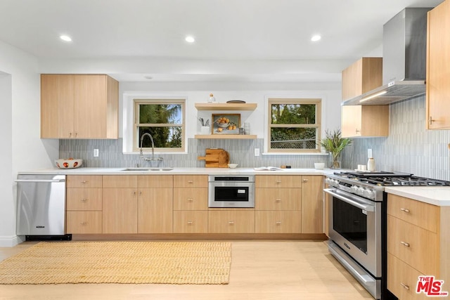 kitchen with wall chimney range hood, sink, appliances with stainless steel finishes, light brown cabinets, and light wood-type flooring