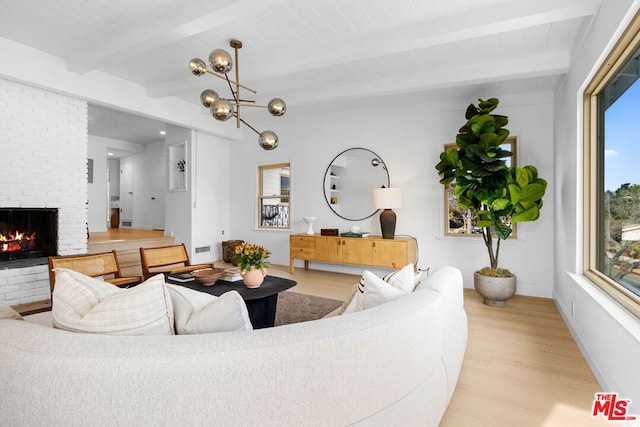 living room featuring beamed ceiling, a brick fireplace, a chandelier, and light hardwood / wood-style flooring