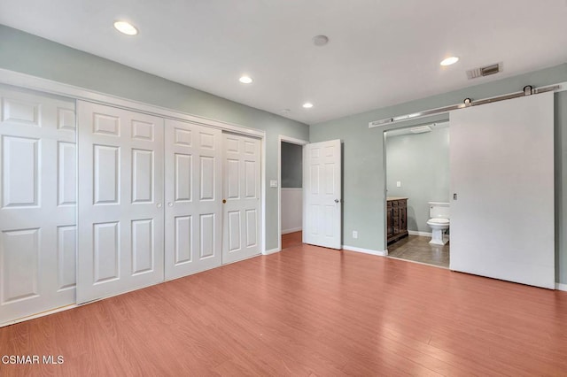 unfurnished bedroom featuring wood-type flooring, a barn door, and ensuite bathroom