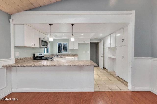 kitchen with hanging light fixtures, kitchen peninsula, stainless steel appliances, light stone countertops, and white cabinets