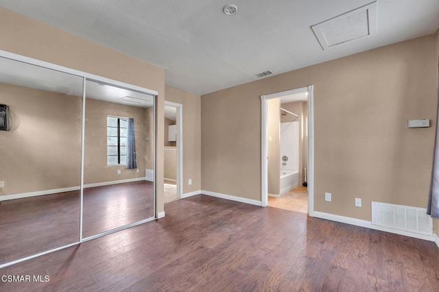 unfurnished bedroom with wood-type flooring, ensuite bath, and a closet