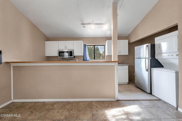 kitchen with white cabinetry, lofted ceiling, stainless steel appliances, and stacked washer and clothes dryer