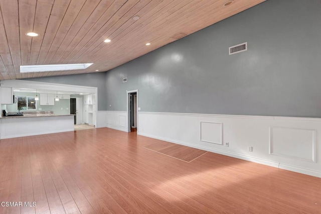 unfurnished living room featuring wooden ceiling, vaulted ceiling with skylight, and light wood-type flooring