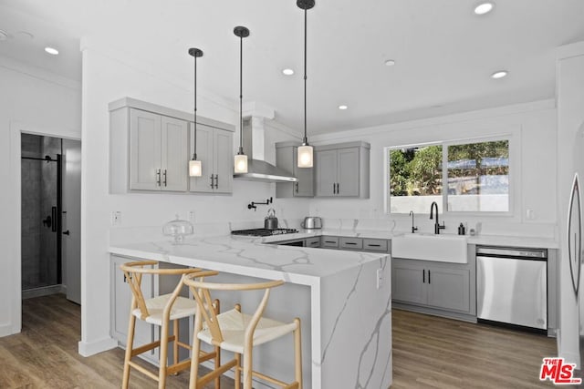 kitchen featuring sink, a breakfast bar area, kitchen peninsula, stainless steel appliances, and wall chimney exhaust hood