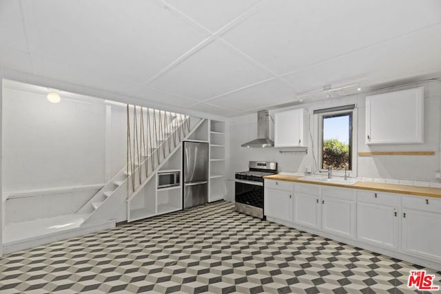 kitchen with wall chimney exhaust hood, butcher block countertops, sink, stainless steel appliances, and white cabinets