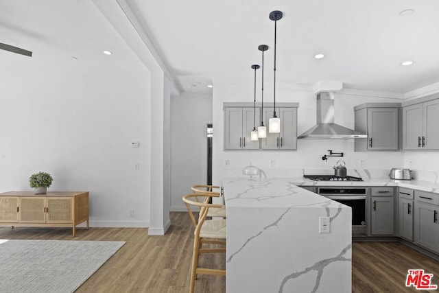 kitchen featuring dark wood-type flooring, wall chimney exhaust hood, sink, pendant lighting, and stainless steel appliances