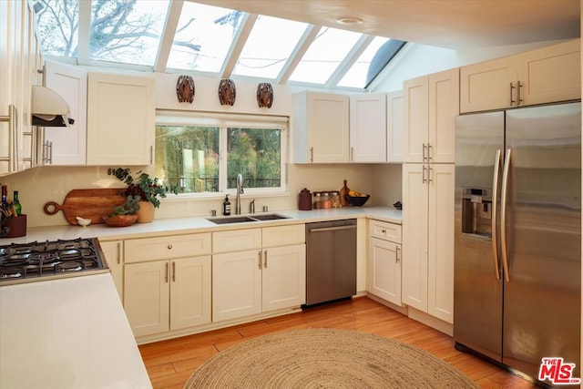 kitchen with sink, appliances with stainless steel finishes, lofted ceiling with skylight, light hardwood / wood-style floors, and a healthy amount of sunlight