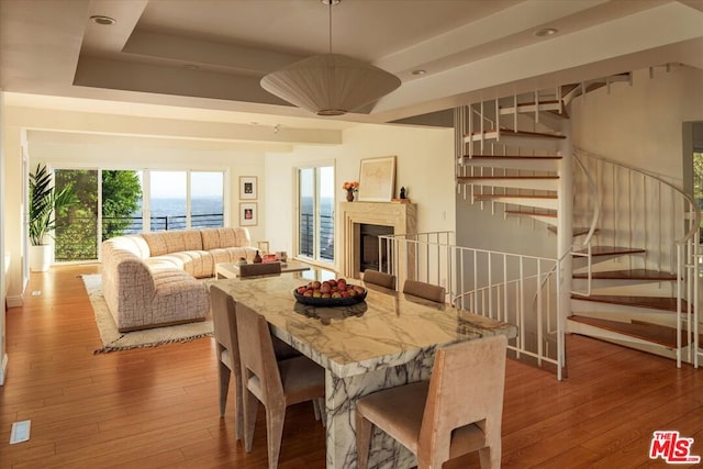 dining space featuring light wood-type flooring, a raised ceiling, and a water view