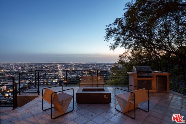 patio terrace at dusk with area for grilling, a fire pit, and exterior kitchen