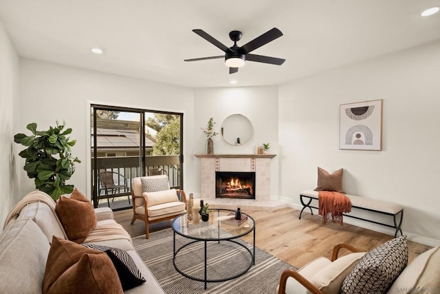 living room with ceiling fan, wood-type flooring, and a tiled fireplace