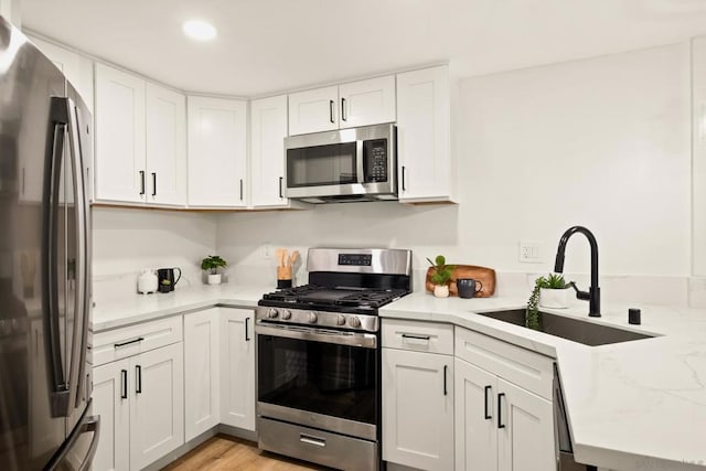 kitchen featuring stainless steel appliances, white cabinetry, sink, and light hardwood / wood-style flooring