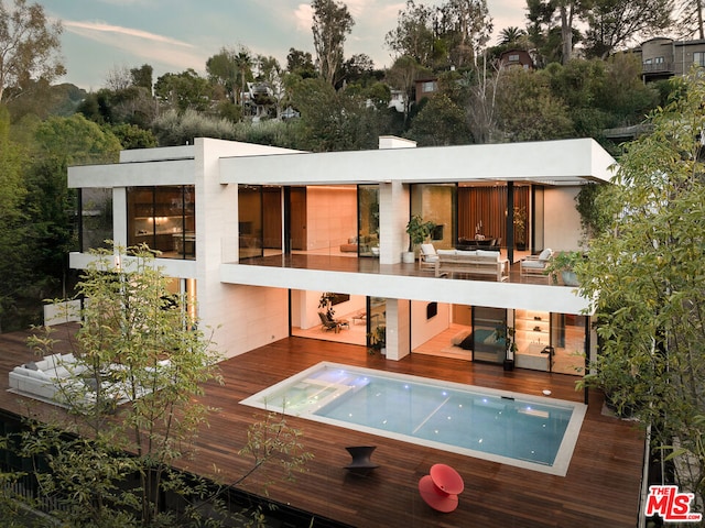 back house at dusk featuring a wooden deck and an outdoor living space