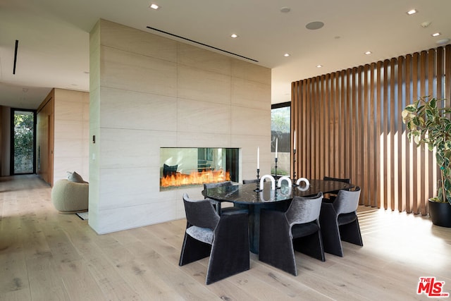 dining area with a tiled fireplace, expansive windows, and light hardwood / wood-style flooring