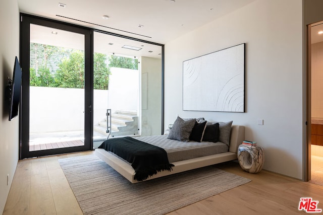 bedroom with light hardwood / wood-style flooring, access to exterior, and a wall of windows