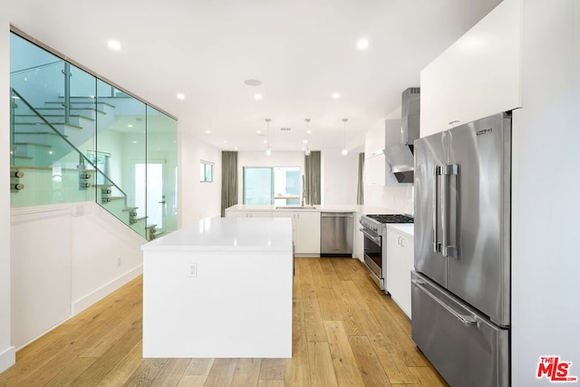 kitchen with white cabinetry, premium appliances, a center island, light wood-type flooring, and wall chimney exhaust hood