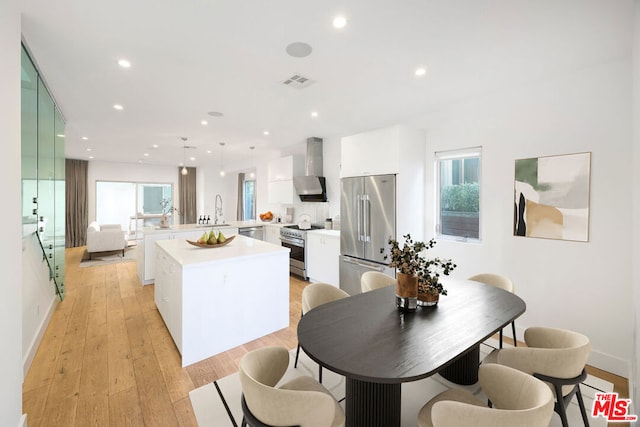 kitchen featuring white cabinetry, decorative light fixtures, premium appliances, a kitchen island, and wall chimney range hood