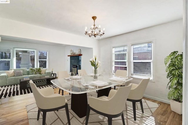 dining room featuring a tiled fireplace, a chandelier, and light wood-type flooring