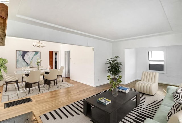 living room featuring wood-type flooring, a tray ceiling, and a notable chandelier