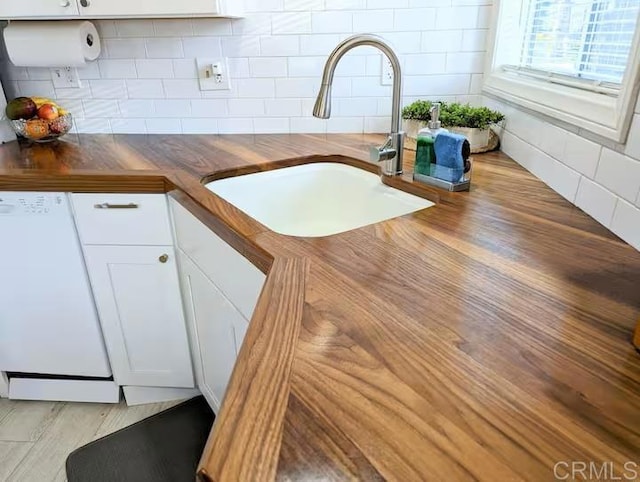 details with dishwasher, butcher block counters, sink, white cabinets, and decorative backsplash