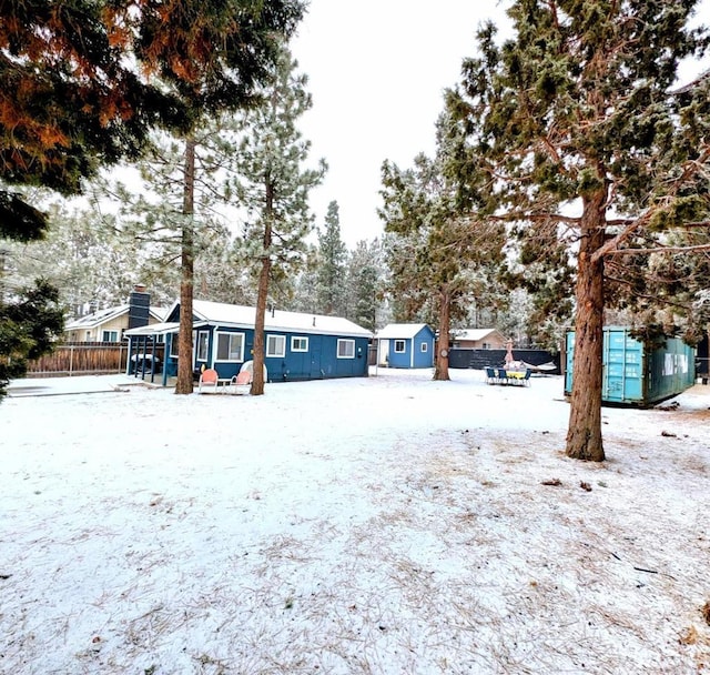 yard layered in snow with a storage unit, an outdoor structure, and fence