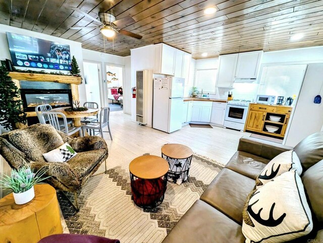 living area featuring a glass covered fireplace, ceiling fan, wooden ceiling, and light wood-style floors