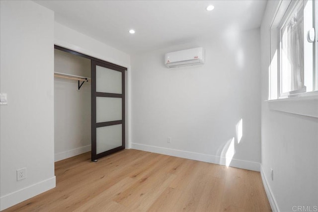 unfurnished bedroom with a wall mounted air conditioner, light hardwood / wood-style floors, and a closet