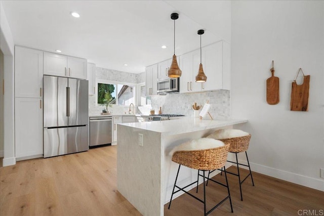 kitchen with stainless steel appliances, decorative light fixtures, white cabinets, and kitchen peninsula