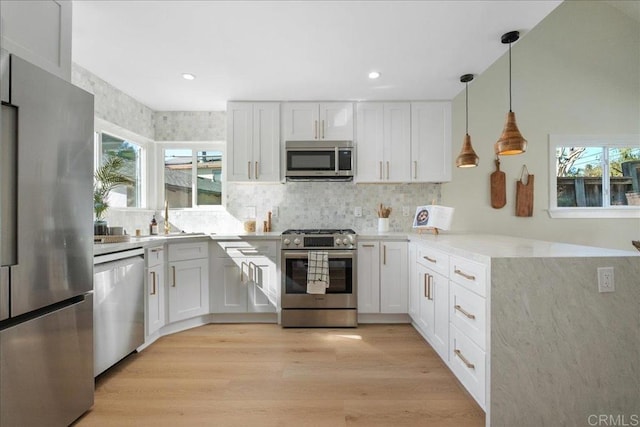 kitchen featuring appliances with stainless steel finishes, white cabinets, light wood-type flooring, and decorative light fixtures