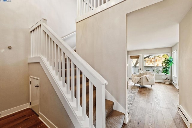 stairway with a baseboard heating unit and hardwood / wood-style floors