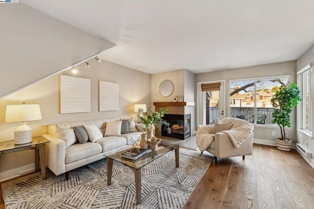 living room with a multi sided fireplace, track lighting, light hardwood / wood-style floors, and a baseboard heating unit