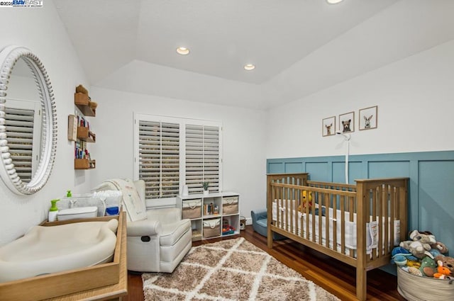 bedroom featuring a nursery area, vaulted ceiling, a raised ceiling, and dark wood-type flooring