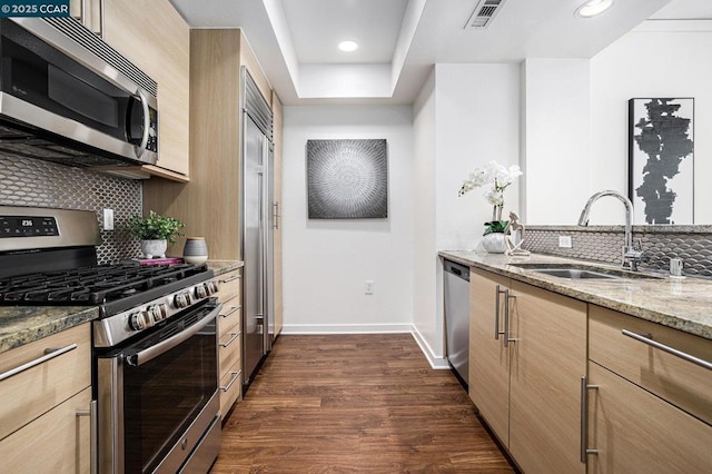 kitchen with sink, dark wood-type flooring, stainless steel appliances, light stone counters, and decorative backsplash