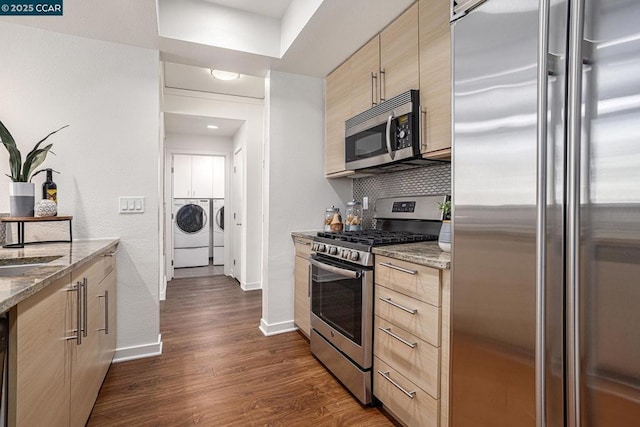 kitchen featuring light stone countertops, appliances with stainless steel finishes, dark hardwood / wood-style floors, and washing machine and clothes dryer