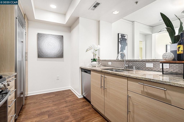 kitchen featuring sink, appliances with stainless steel finishes, dark hardwood / wood-style flooring, light stone countertops, and decorative backsplash