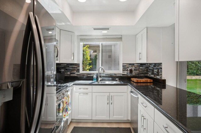 kitchen with white cabinetry, sink, stainless steel appliances, and dark stone countertops