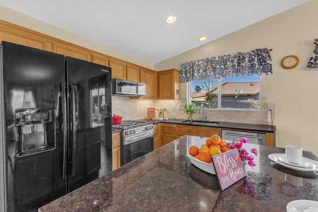 kitchen featuring sink, vaulted ceiling, dark stone countertops, appliances with stainless steel finishes, and backsplash