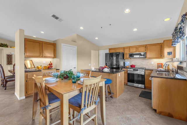 kitchen featuring sink, light tile patterned floors, appliances with stainless steel finishes, backsplash, and a kitchen island