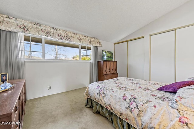 carpeted bedroom with vaulted ceiling, a textured ceiling, and two closets