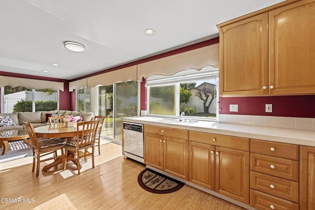 kitchen with stainless steel dishwasher, tile counters, sink, and light hardwood / wood-style flooring