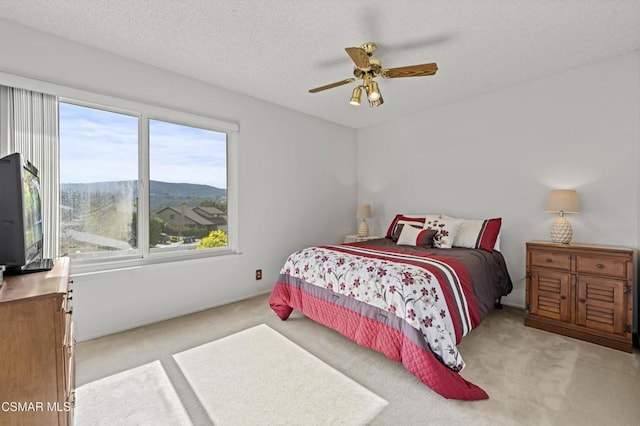 bedroom with ceiling fan, a mountain view, light carpet, and a textured ceiling