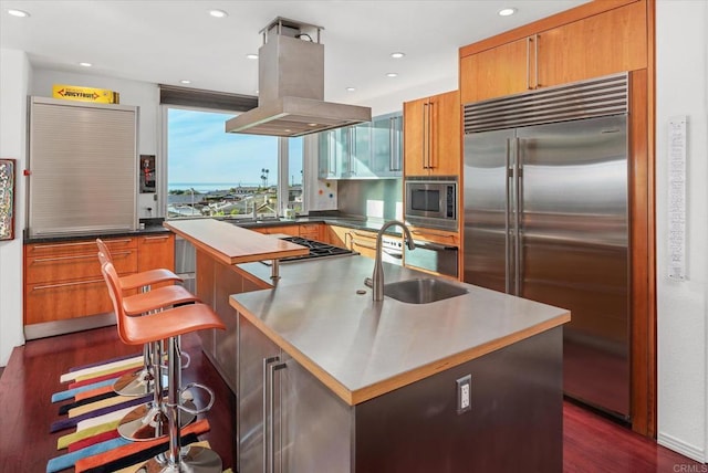 kitchen featuring sink, a kitchen breakfast bar, a center island, built in appliances, and island range hood