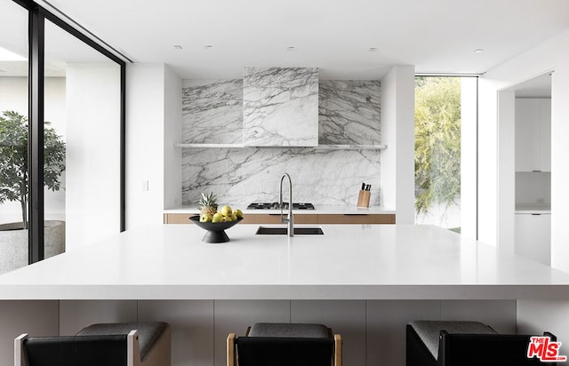 kitchen with a breakfast bar, sink, backsplash, expansive windows, and gas stovetop