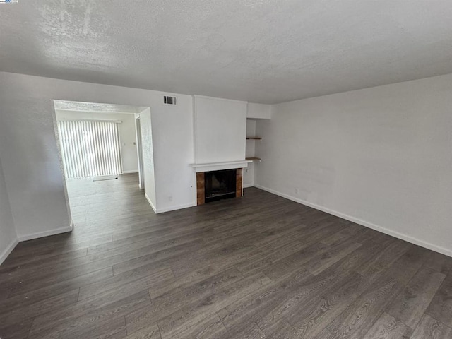 unfurnished living room featuring dark hardwood / wood-style floors, a tiled fireplace, and a textured ceiling