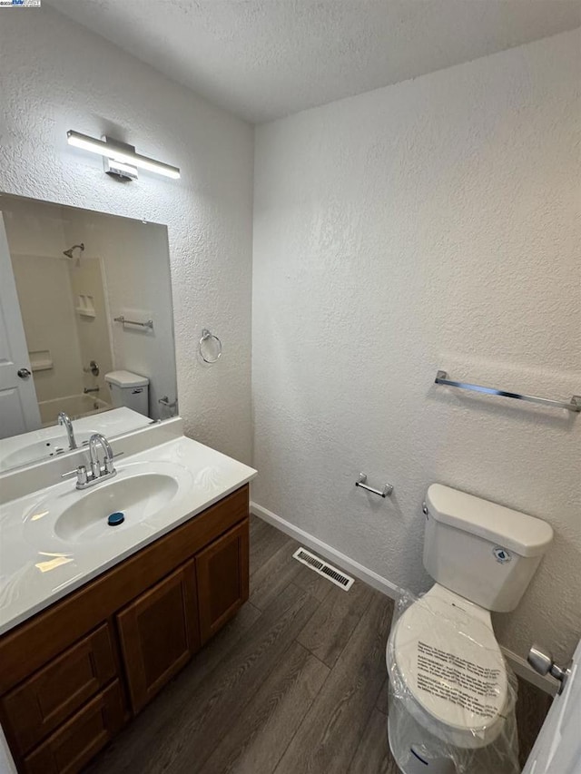 full bathroom with hardwood / wood-style floors, vanity, a textured ceiling, bathtub / shower combination, and toilet