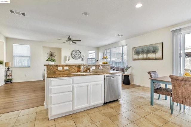 kitchen featuring sink, light tile patterned floors, stainless steel dishwasher, dark stone counters, and white cabinets