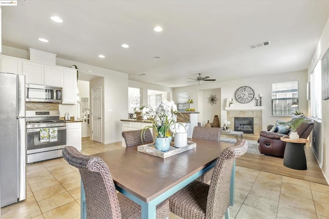 dining space with ceiling fan, a fireplace, and light tile patterned floors