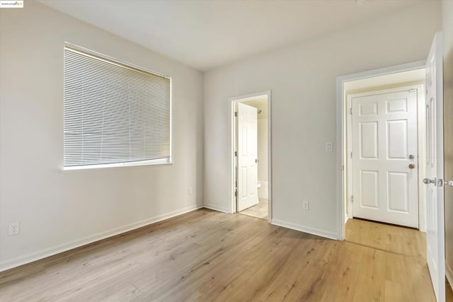 unfurnished bedroom with connected bathroom and light wood-type flooring