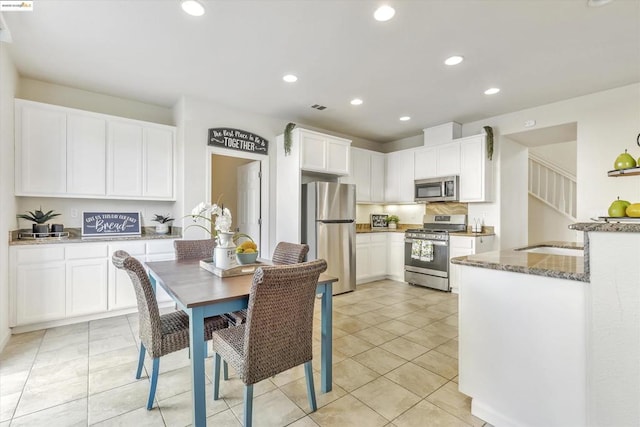 kitchen with light tile patterned floors, sink, appliances with stainless steel finishes, white cabinets, and dark stone counters